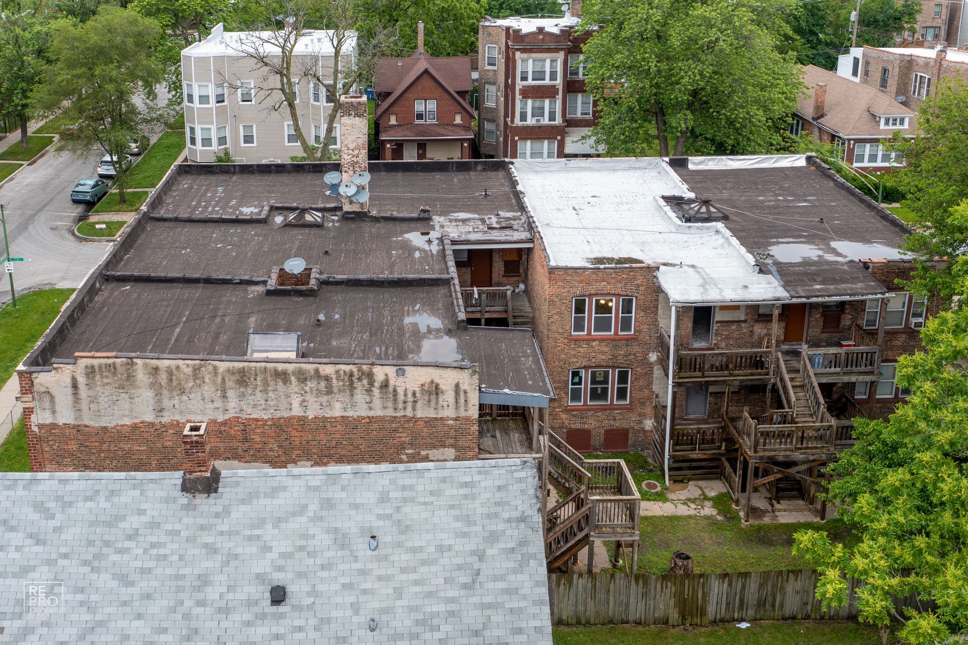 Aerial view of dilapidated brick buildings with aging roofs and wooden exteriors; surrounding greenery.
