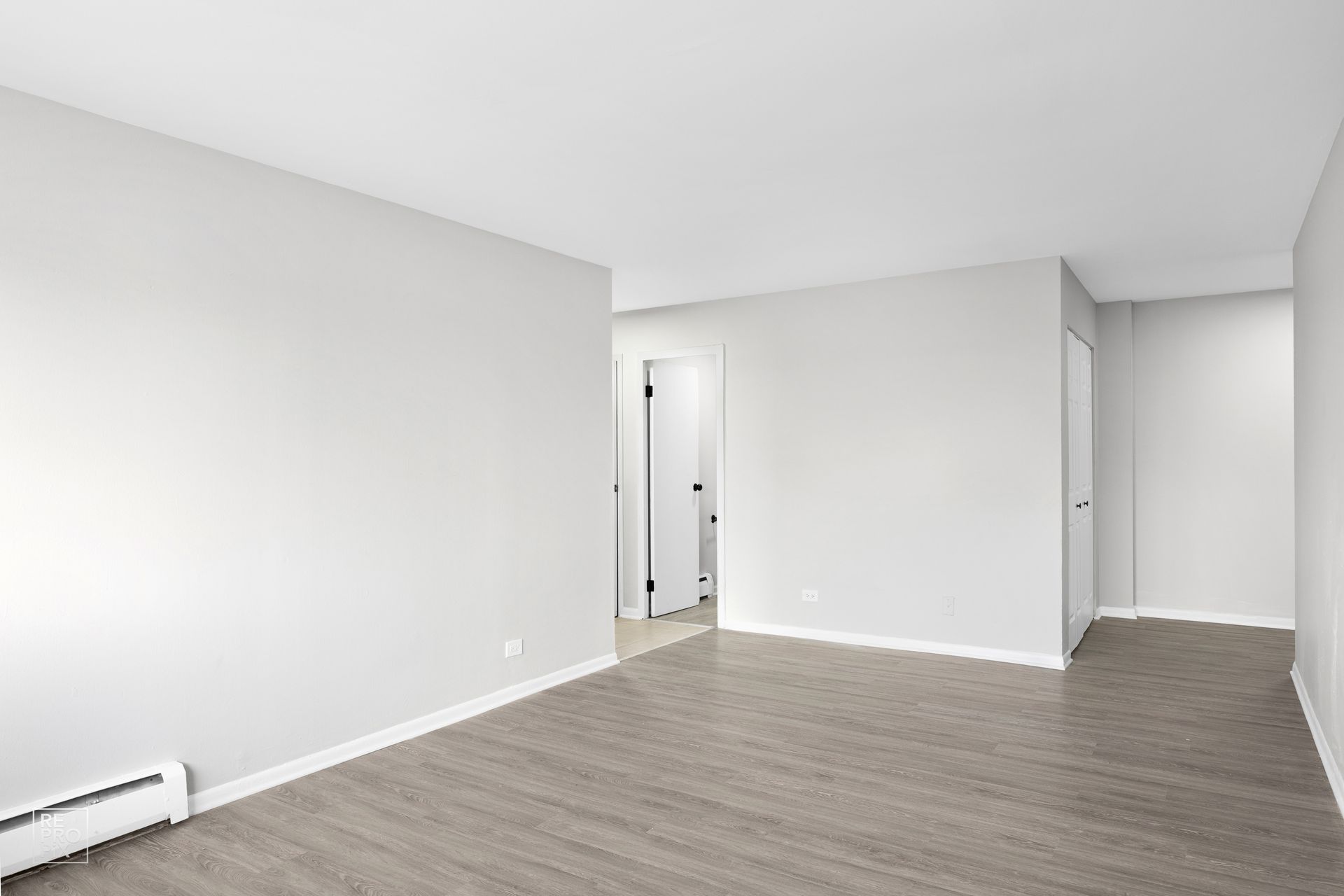 Empty room with gray walls and wood-look flooring. Two doorways, one open to a hallway.