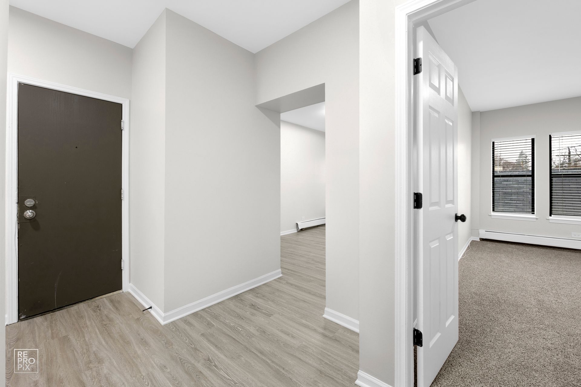 Empty hallway with a brown door, doorway, and room with windows.