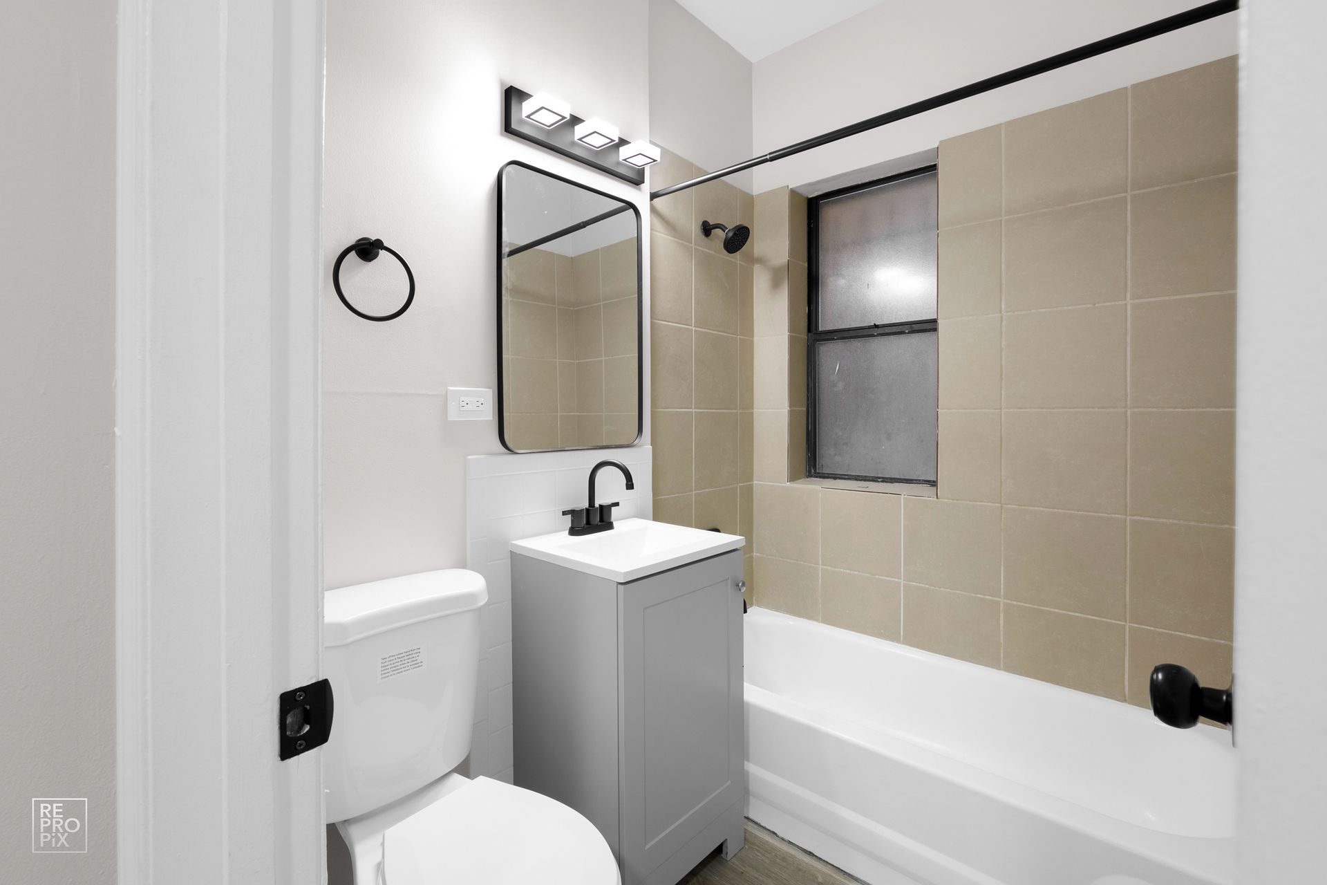 Bathroom with white and tan tiles, black fixtures, and a vanity.