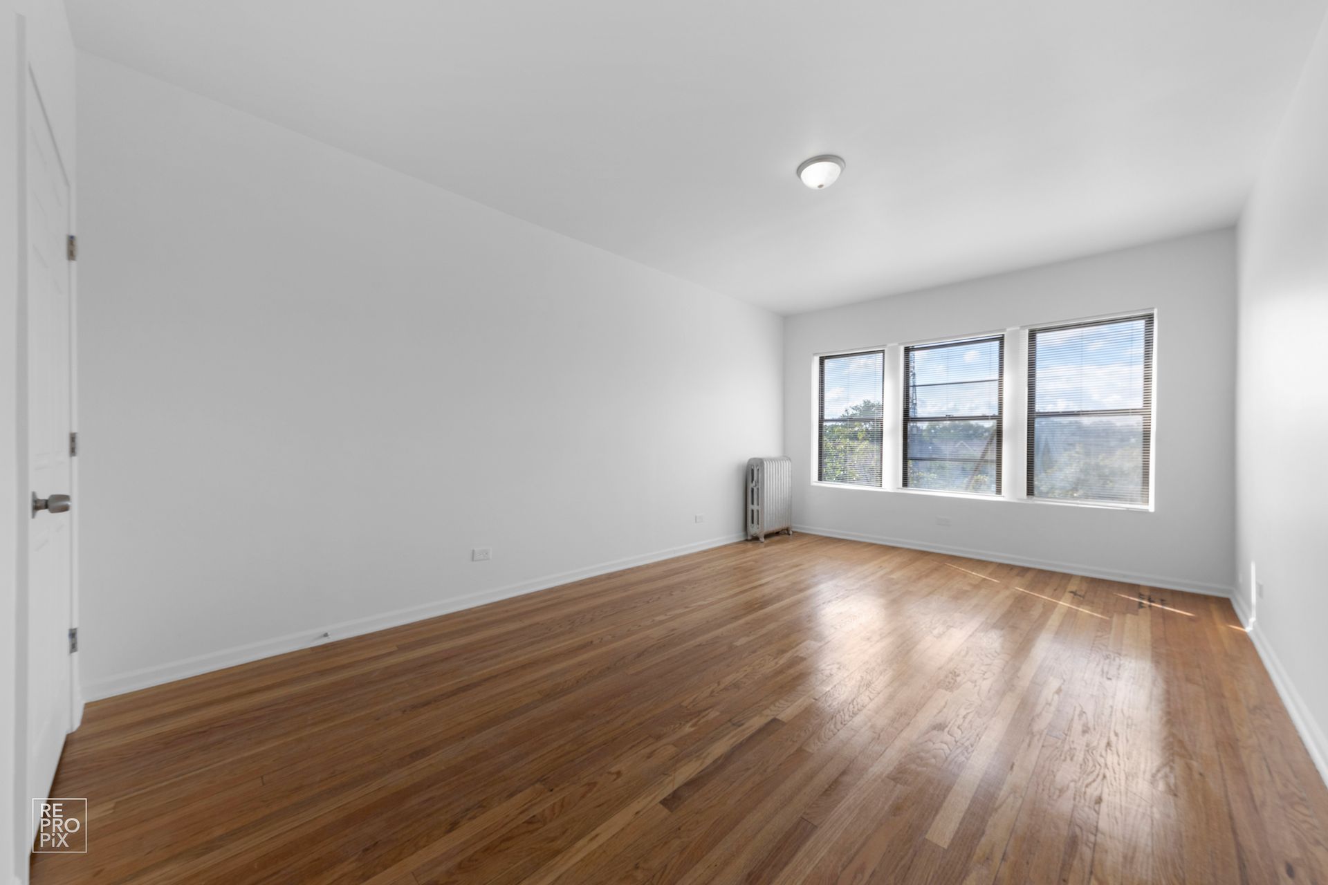 Empty room with hardwood floors, white walls, and a window with a view.