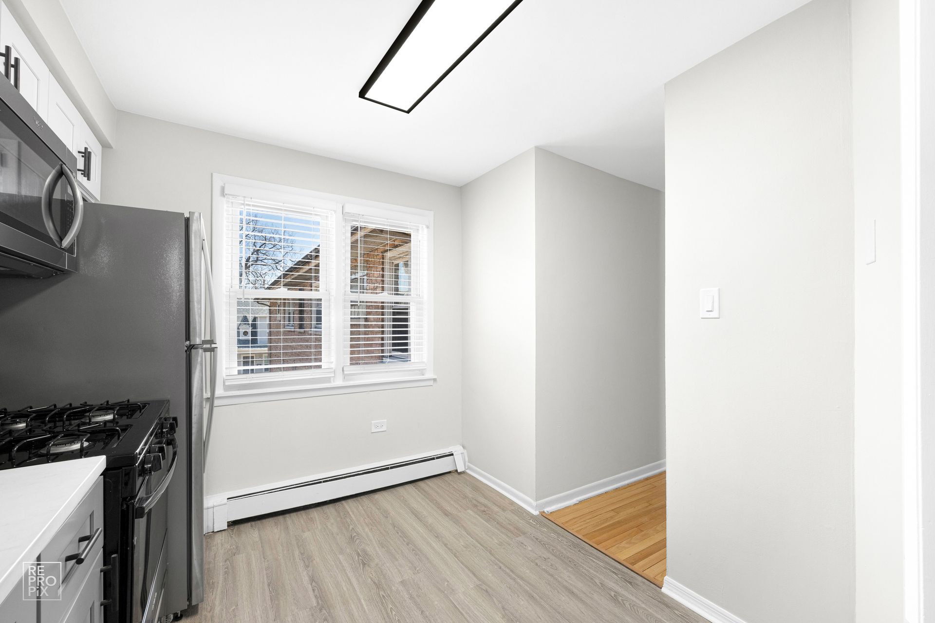 Kitchen with gray appliances, window, and wood-look flooring. Light gray walls and white trim.