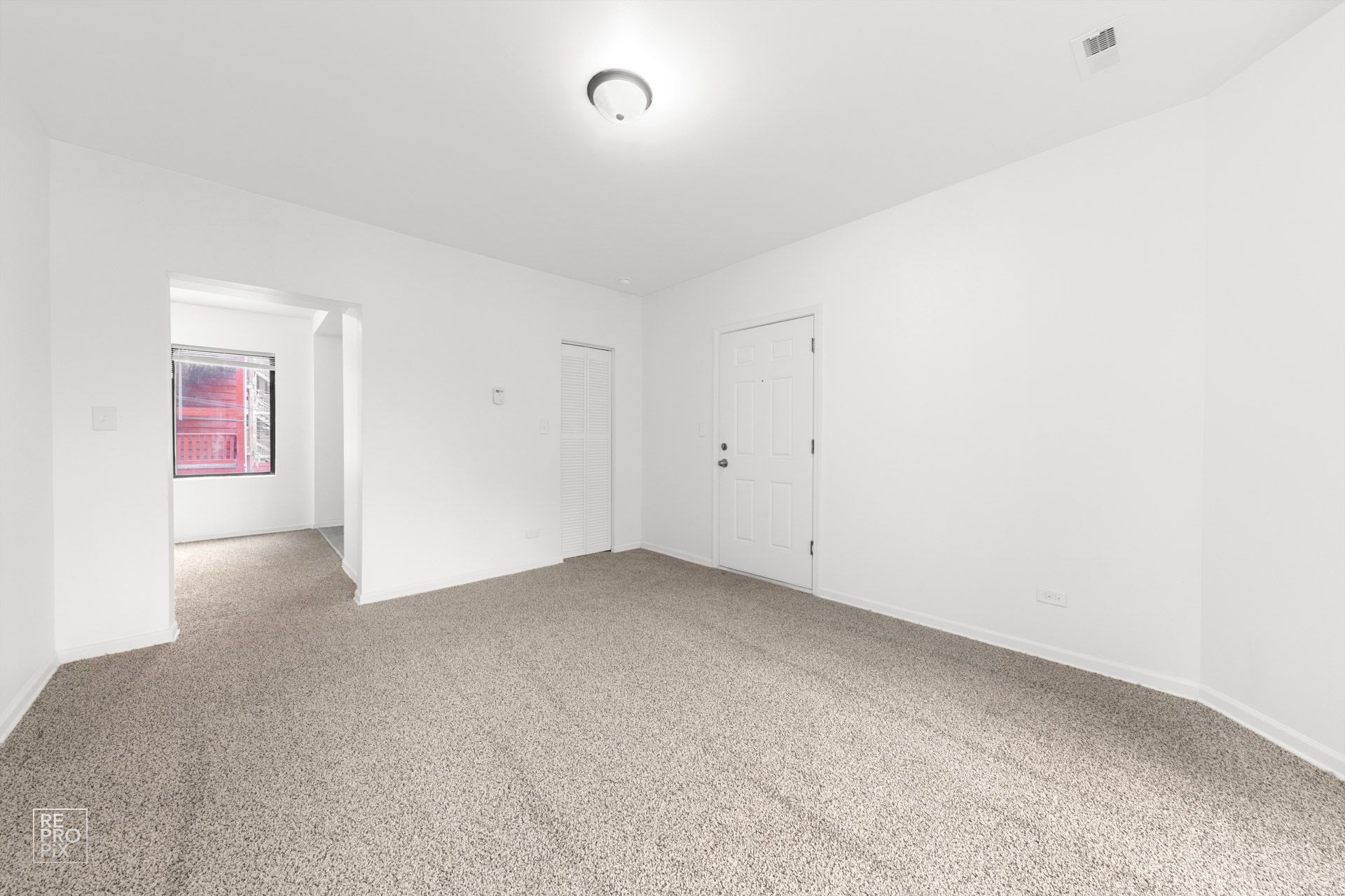 Empty room with beige carpet and white walls, doorway to another room with window.