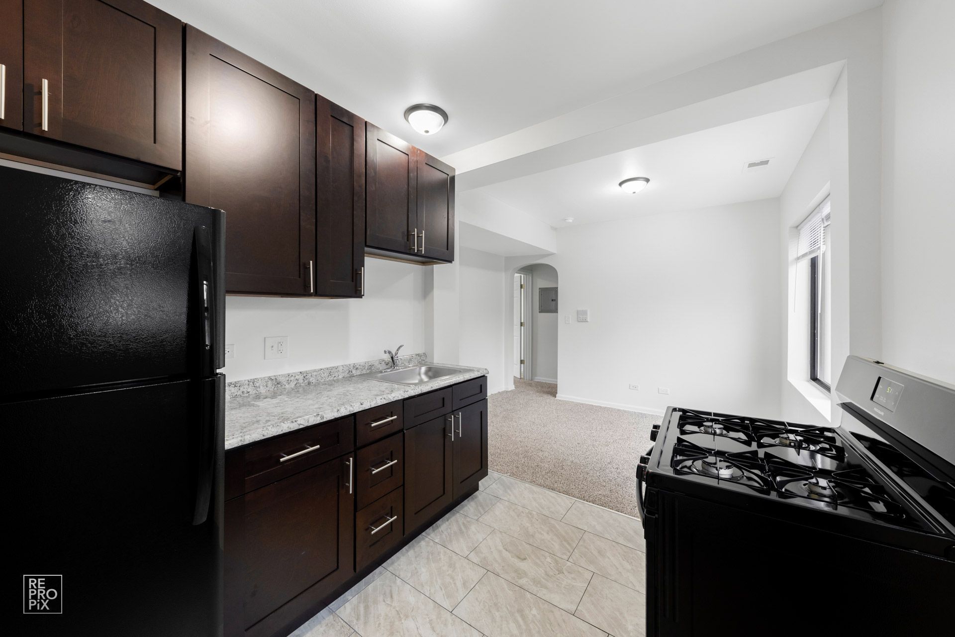 Kitchen with dark cabinets, black appliances, and a light-colored countertop.