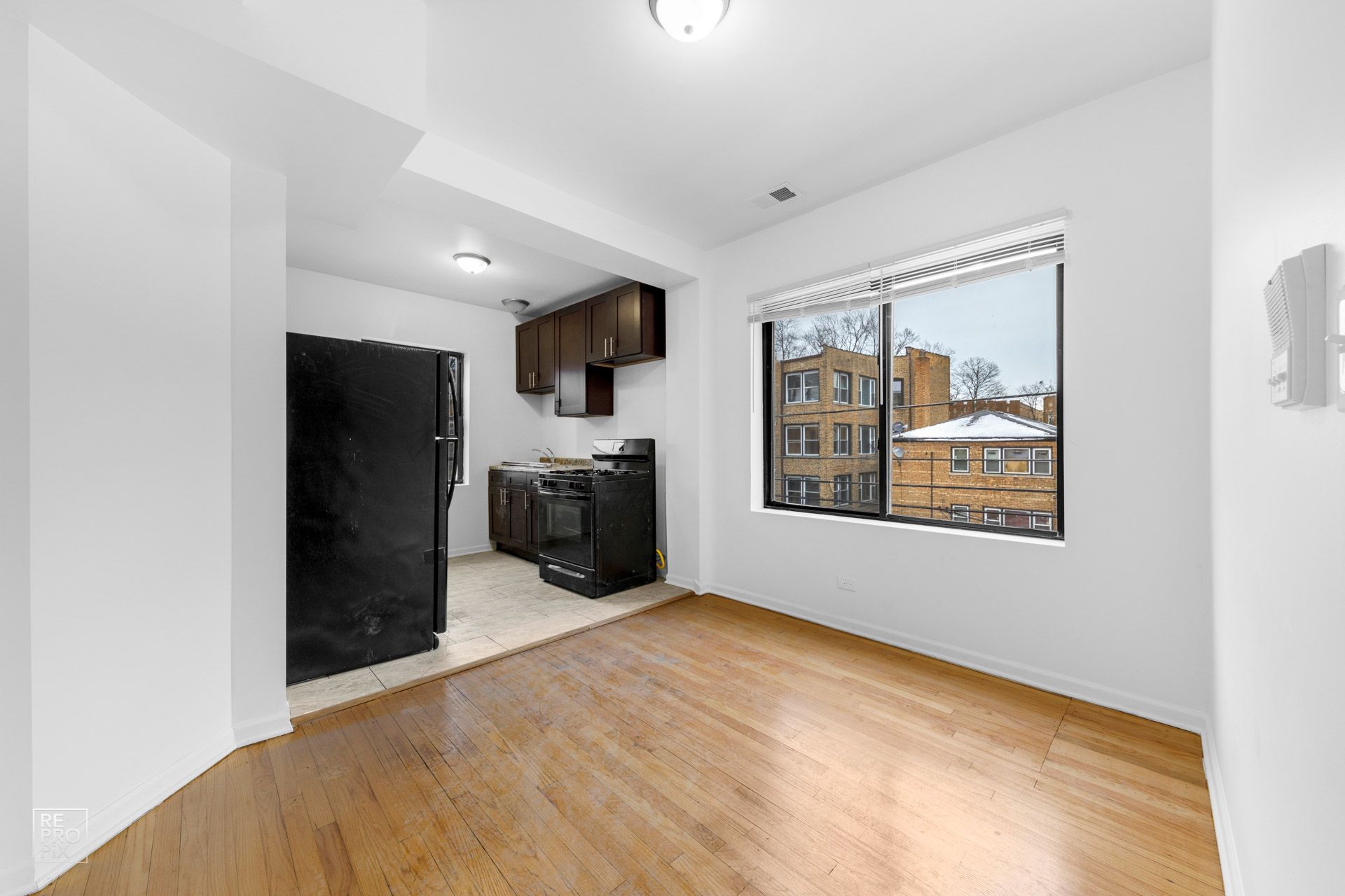 Empty apartment interior with kitchen, black appliances, and a window with a building view.