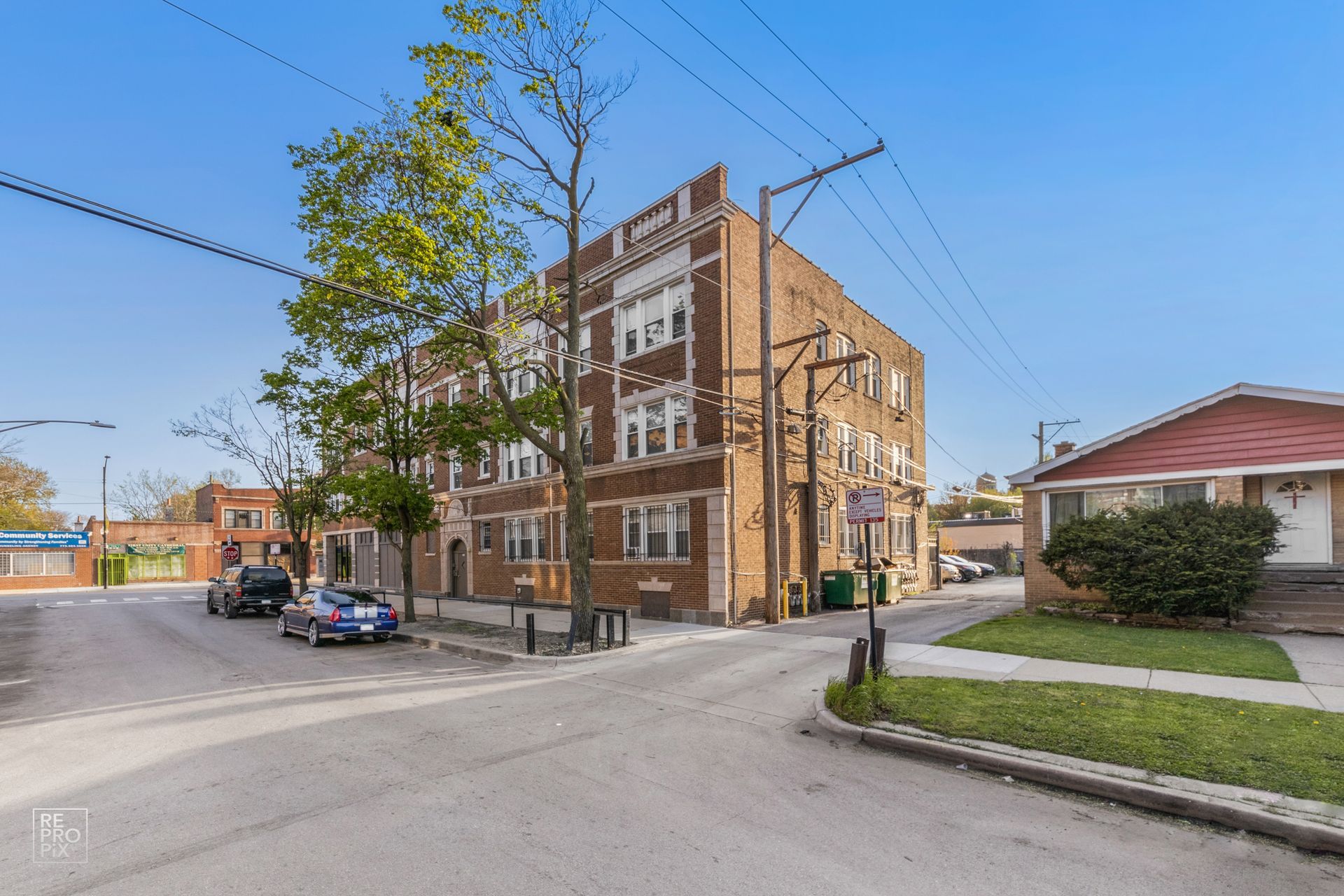 Brick apartment building on a street corner, cars parked nearby. Sunny day, blue sky.