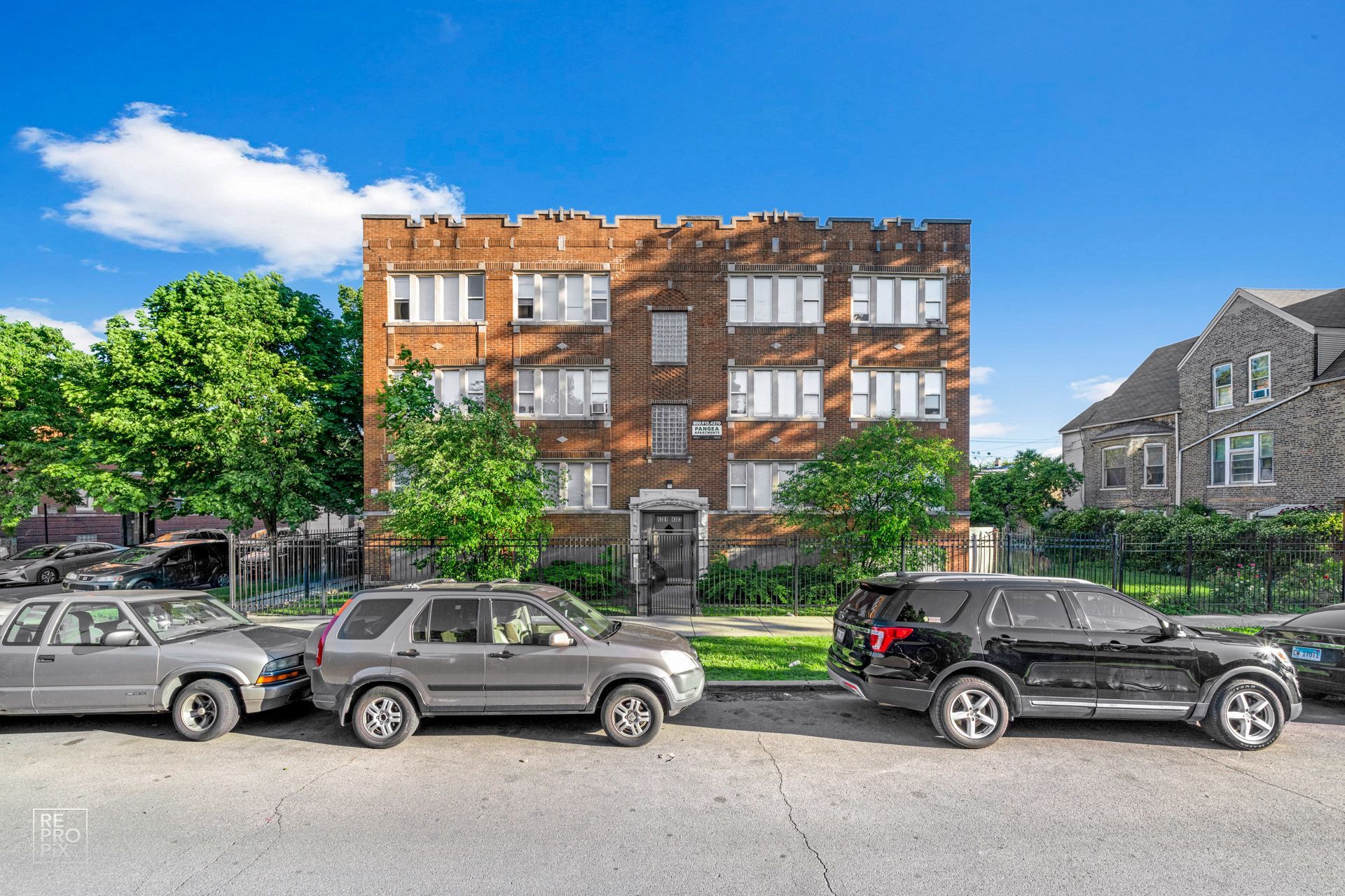 Apartment building facade with parked cars on street, sunny day.