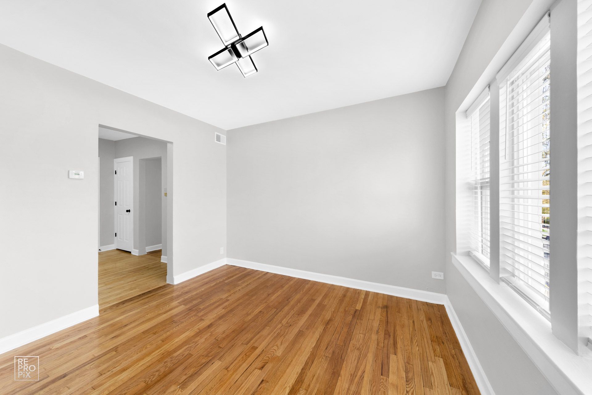 Empty room with hardwood floors, white walls, and a window with blinds.