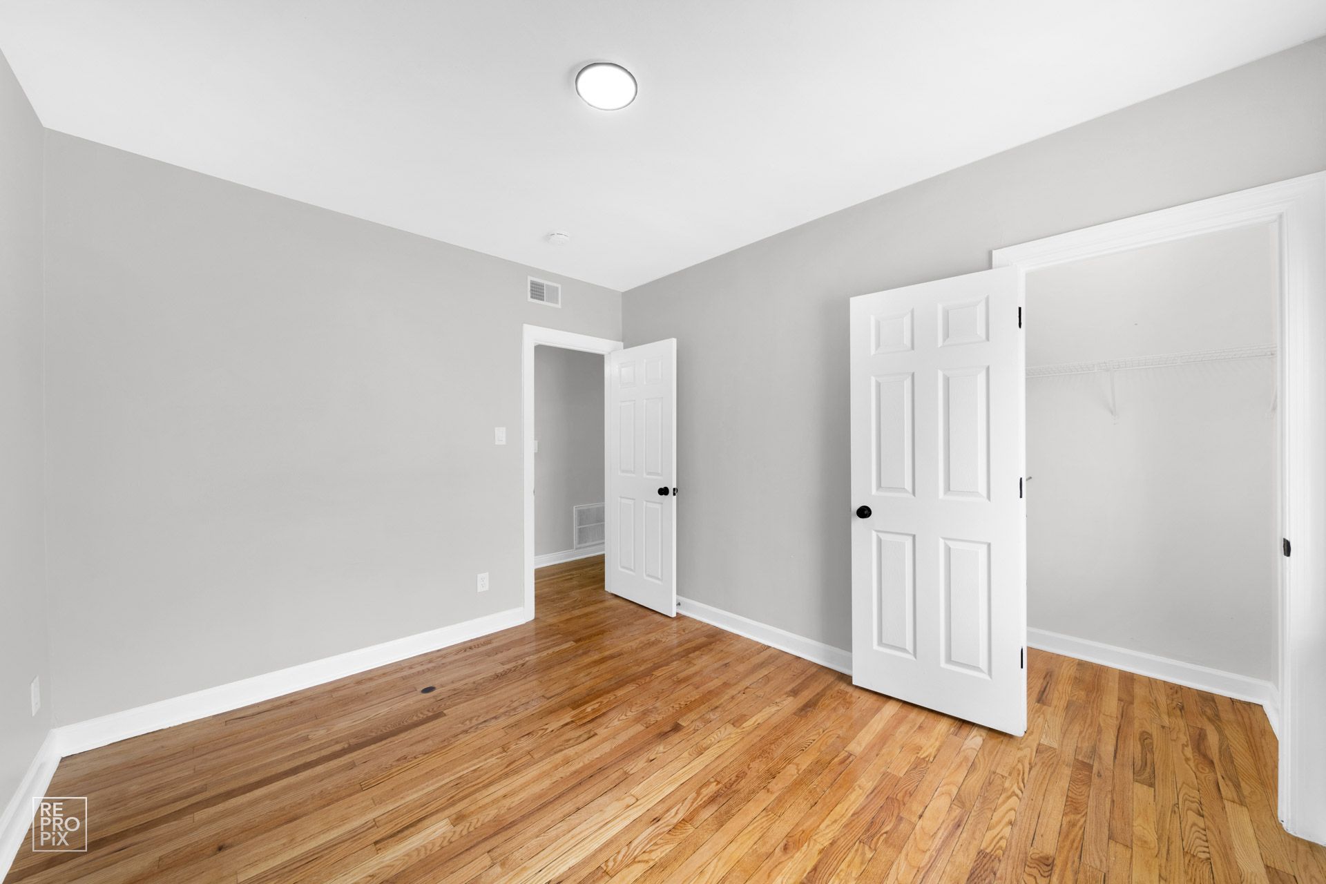 Empty bedroom with gray walls, hardwood floor, white doors, and a closet.
