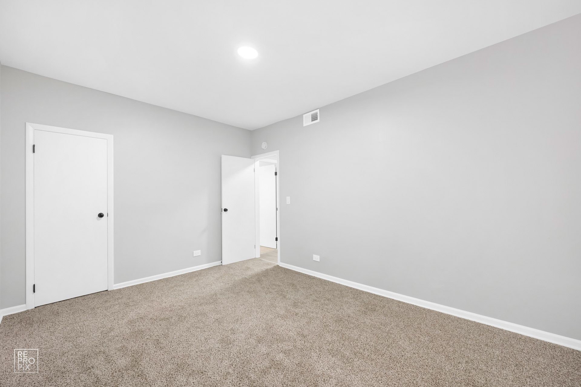 Empty bedroom with gray walls, two white doors, and light brown carpet.