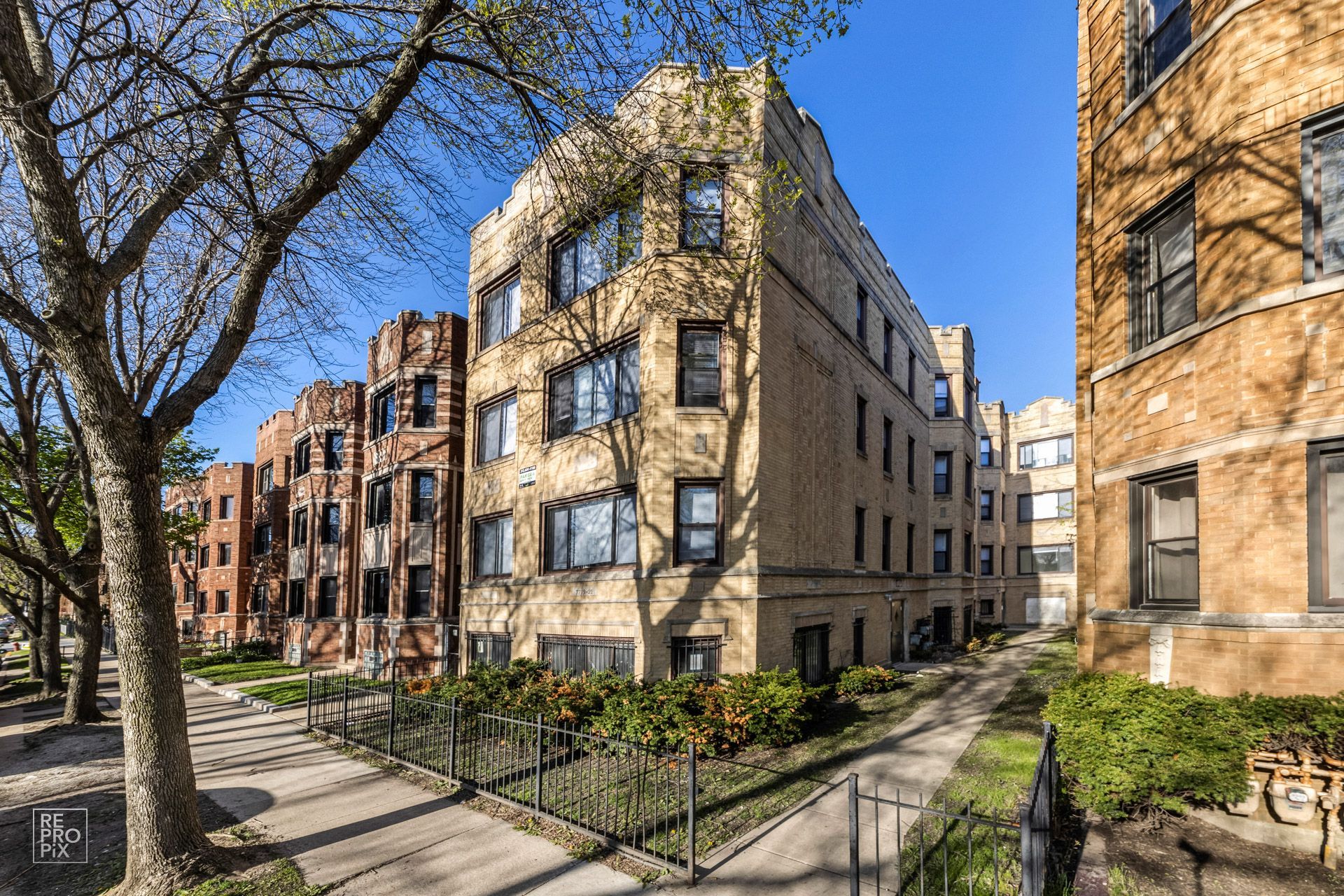 Multi-story brick apartment buildings with trees and a sidewalk on a sunny day.