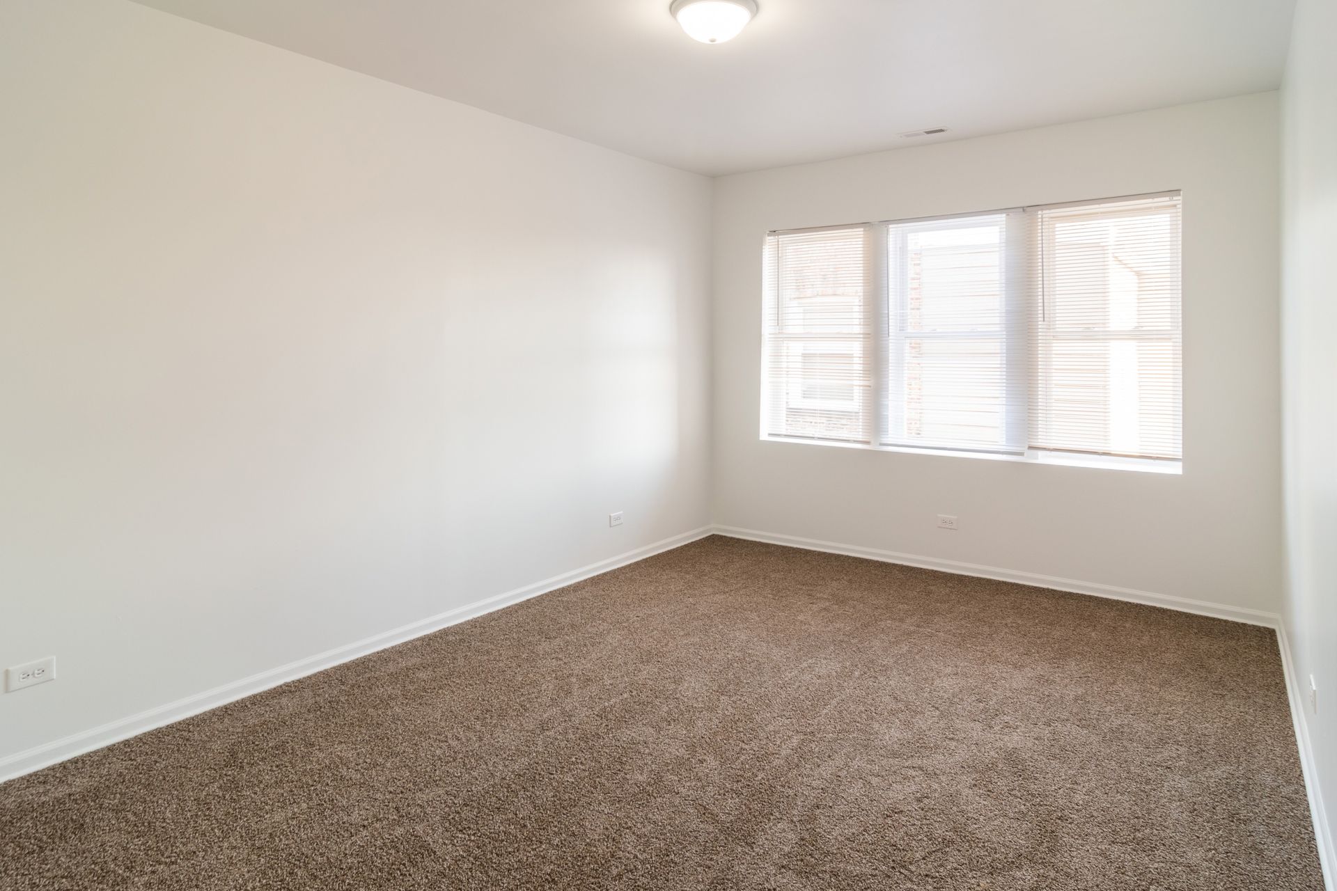 Empty room with brown carpet, white walls, a window with blinds, and a ceiling light.