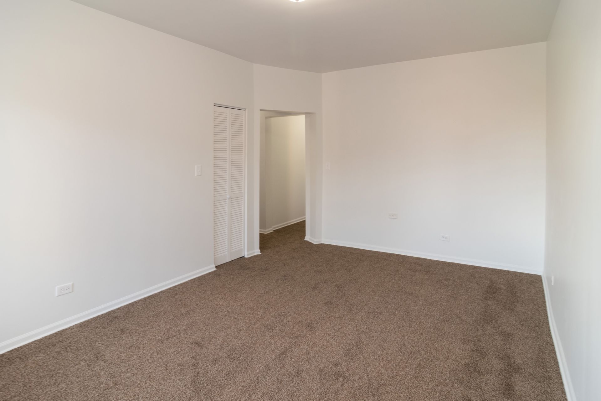 Empty room with brown carpet, white walls, and an open doorway.
