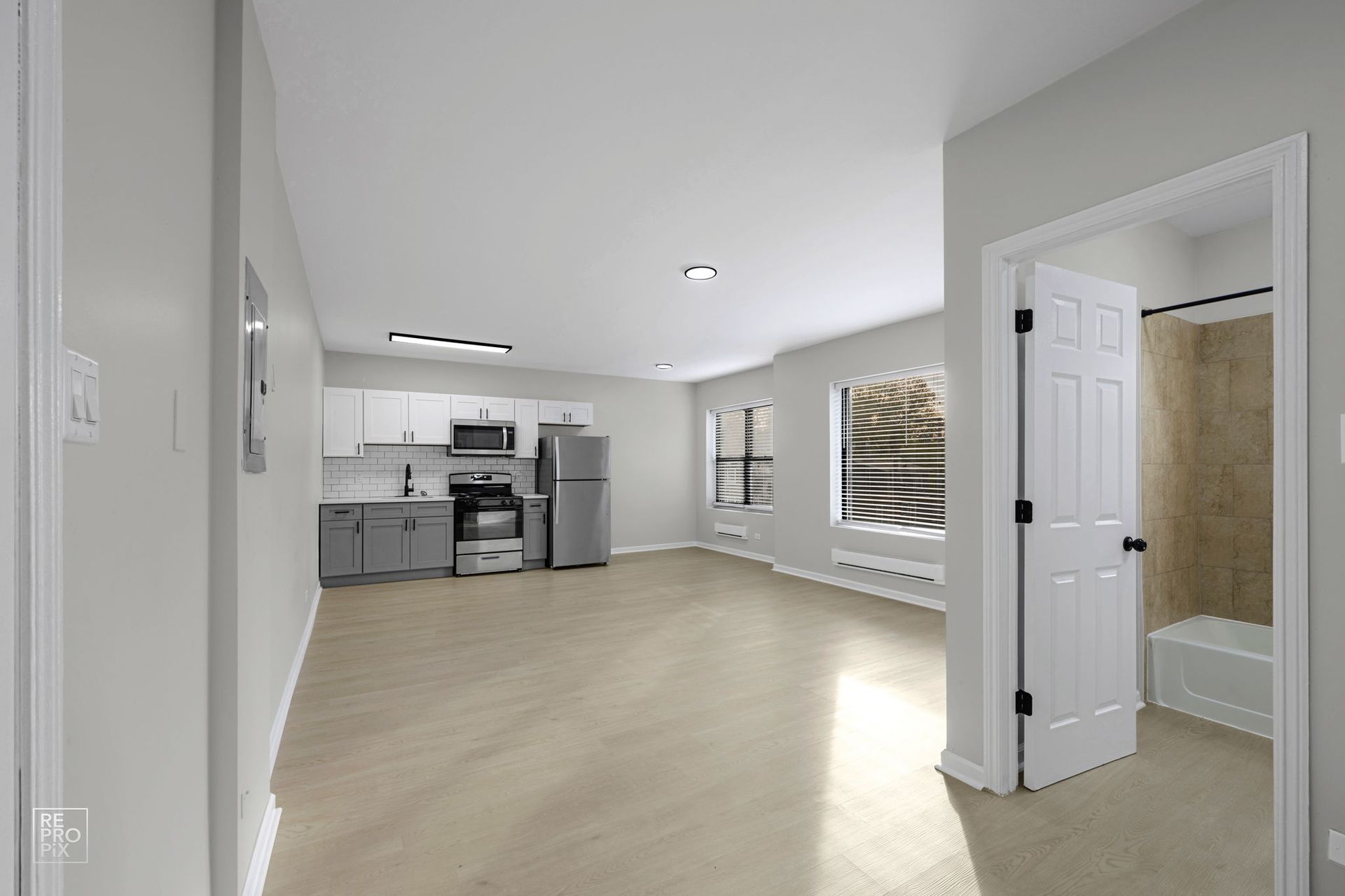 Empty apartment interior with kitchen, living area, and bathroom doorway. Neutral colors and natural light.