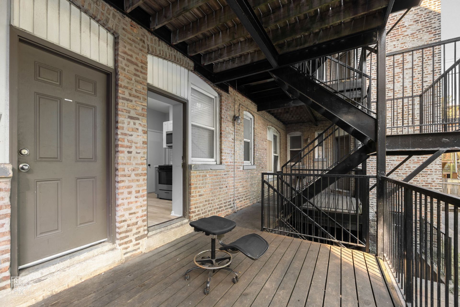 Exterior view of a brick building with a wooden deck, black metal fire escape, and an open doorway.