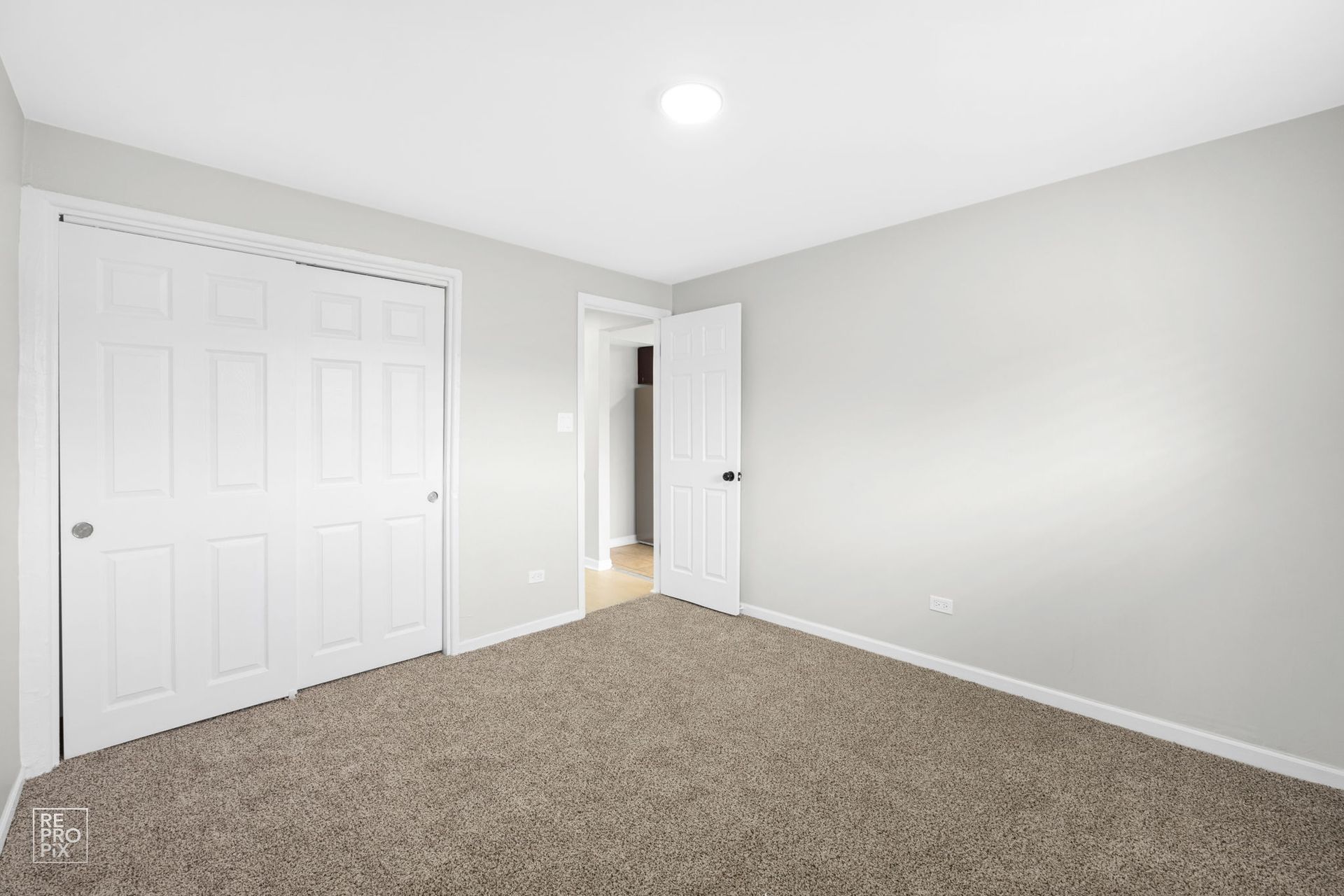 Empty bedroom with gray walls, white closet doors, and beige carpet.