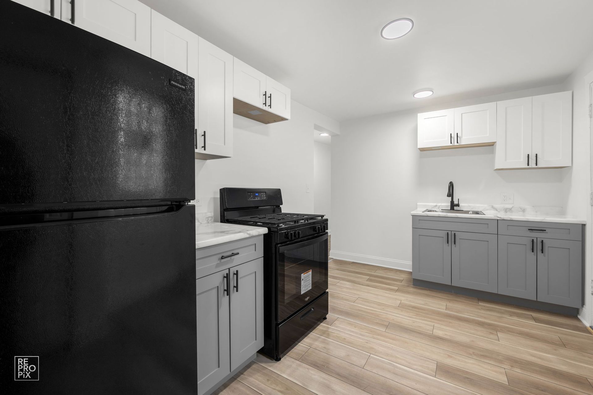 Modern kitchen with black appliances, white and gray cabinets, and light wood flooring.
