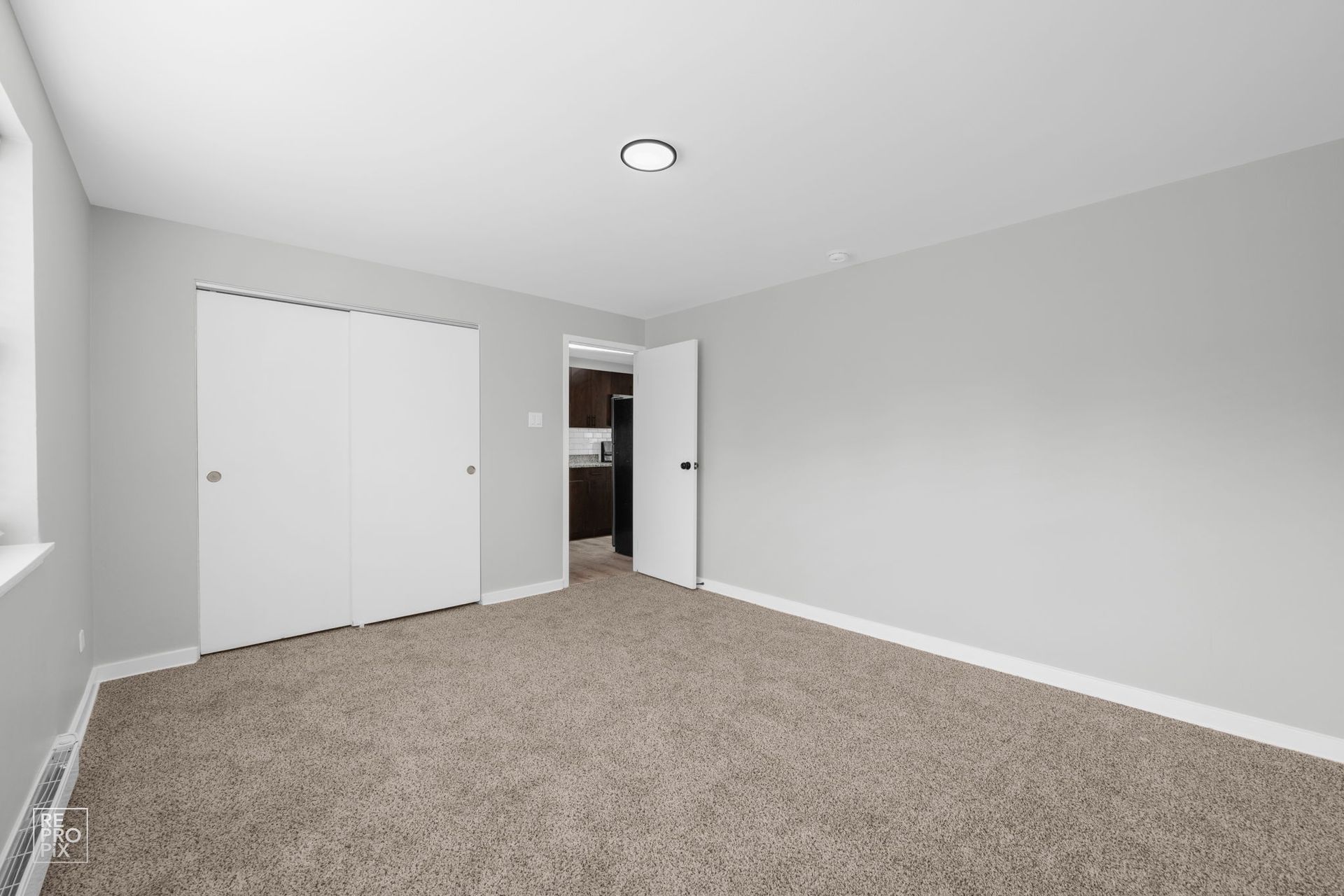 Empty bedroom with gray walls, beige carpet, white closet doors, and open door to another room.
