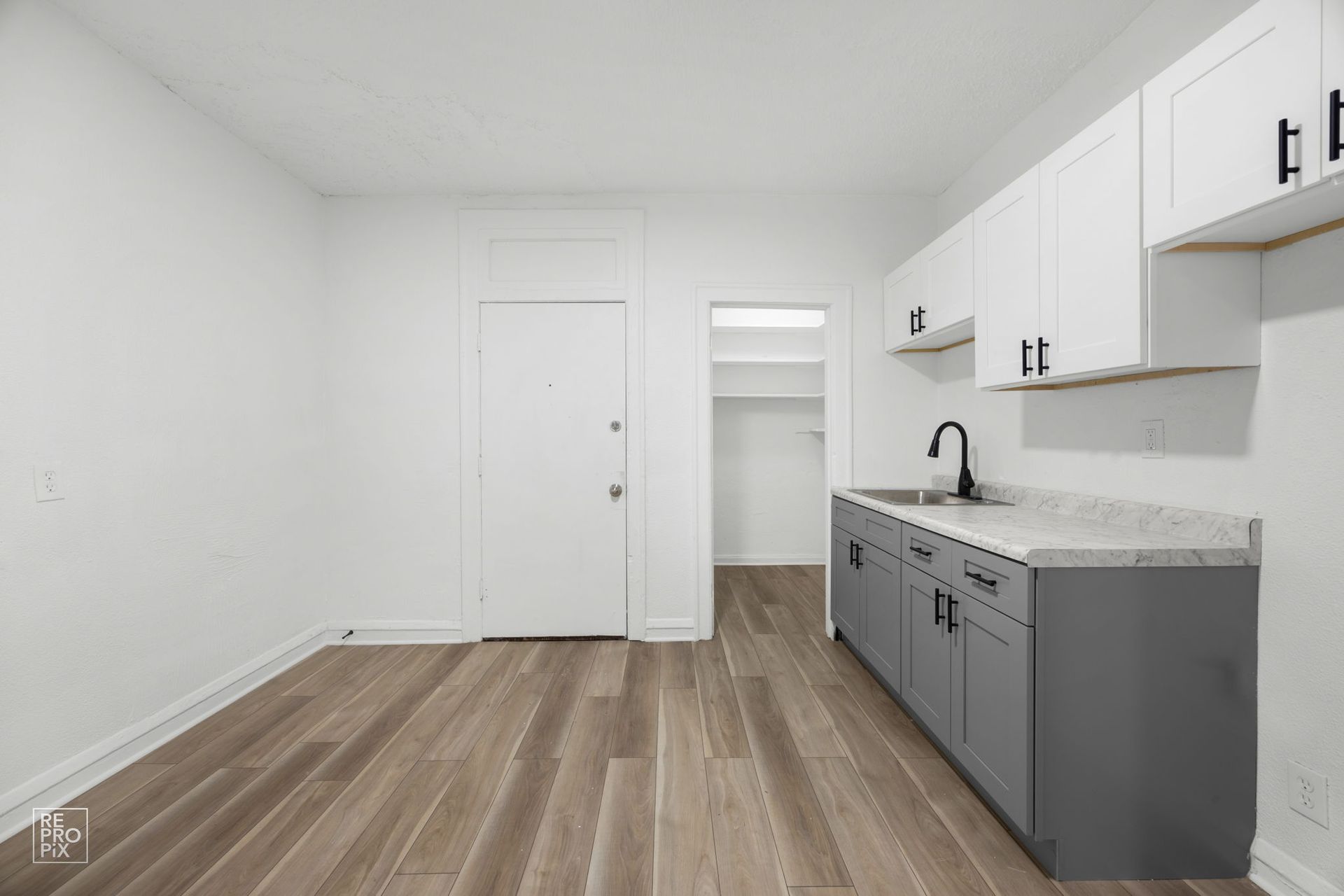 Empty studio apartment with kitchen cabinets, sink, and open doorway to closet.