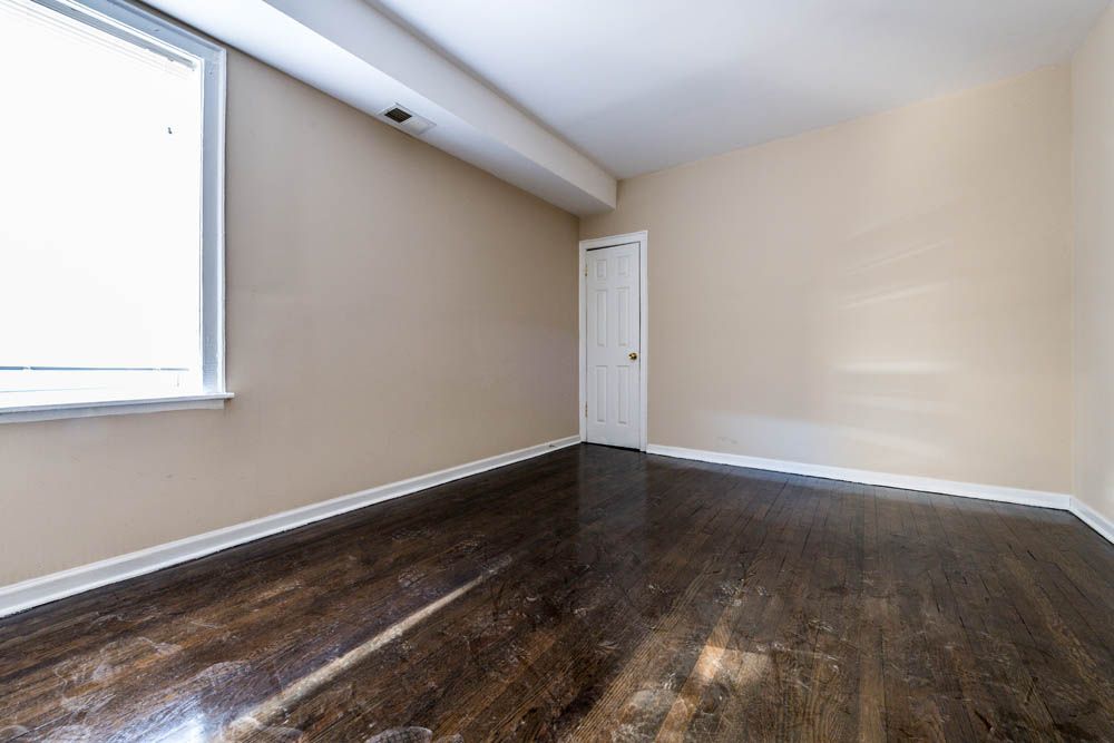 Empty room with dark wood floor, tan walls, window, and white door.