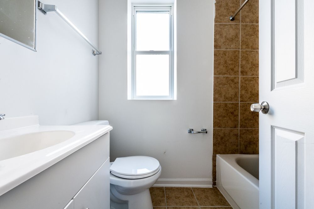 Bathroom with white vanity, toilet, and bathtub. Brown tile shower wall, small window.