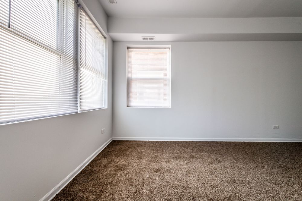 Empty room with carpet, three windows with blinds, and white walls.