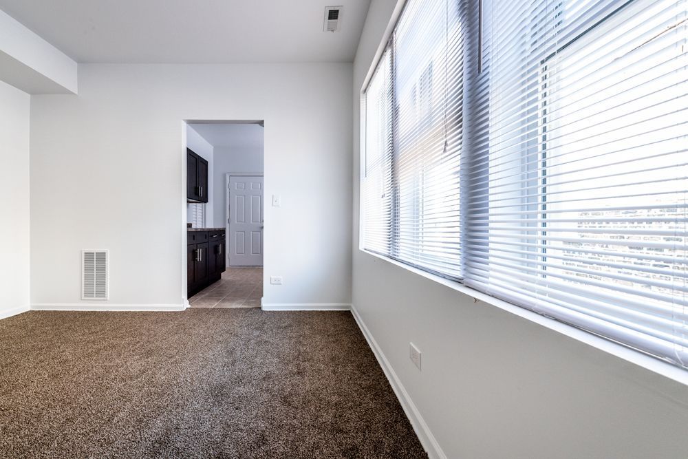 Empty room with brown carpet, white walls, and a large window with blinds.