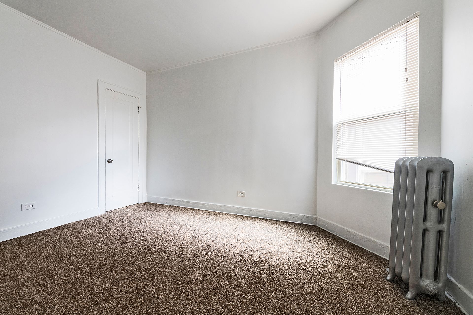 Empty room with brown carpet, white walls, a window, and a radiator.