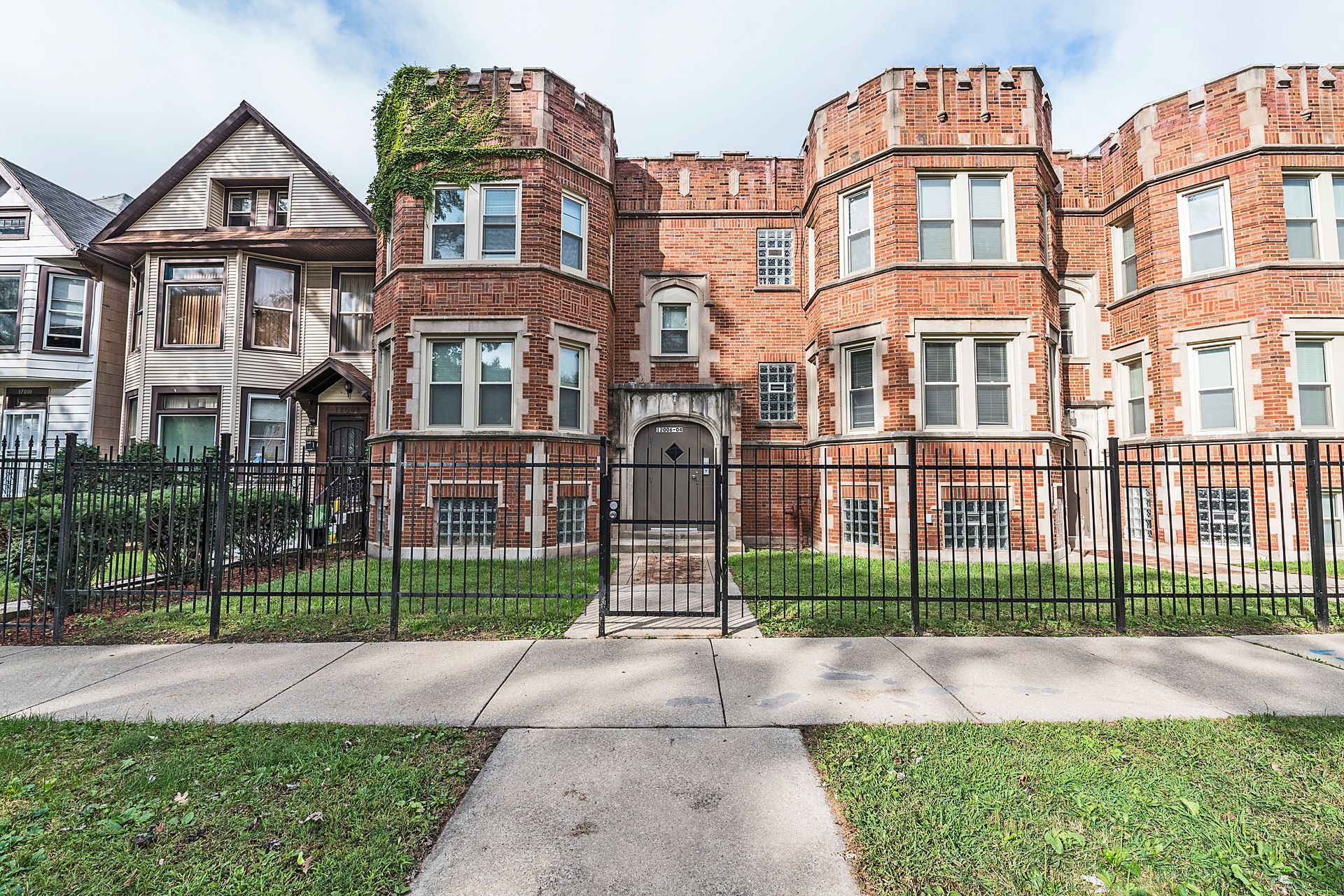 Brick apartment building with decorative turrets and a wrought-iron fence.