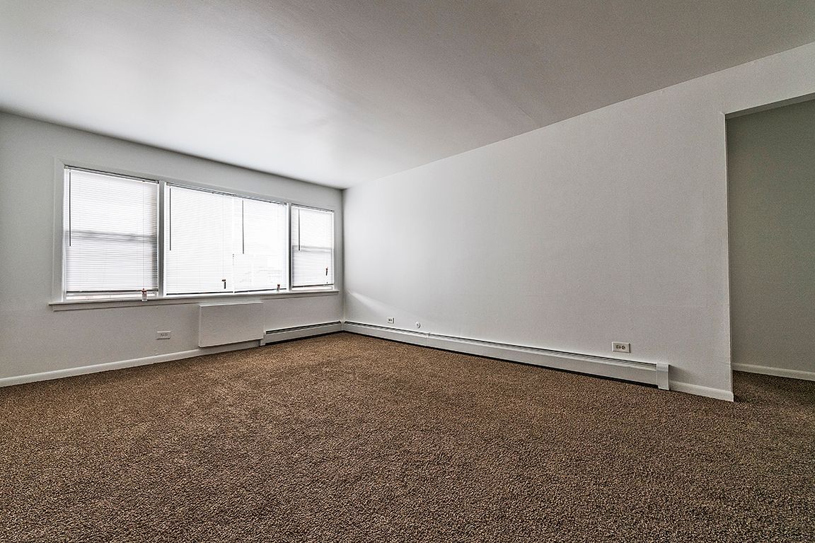 Empty room with brown carpet, white walls, a window, and a radiator.