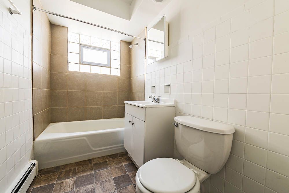 Bathroom with white toilet, vanity, and bathtub; brown tiled walls and floor.