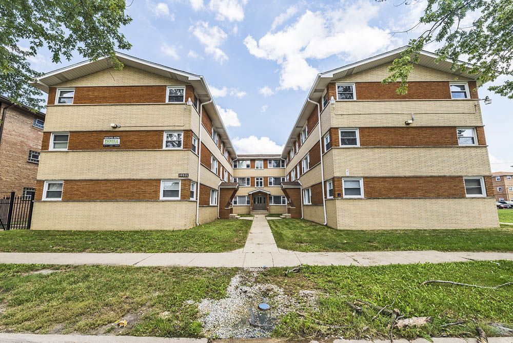 Multi-story brick apartment building with beige siding under a blue sky.
