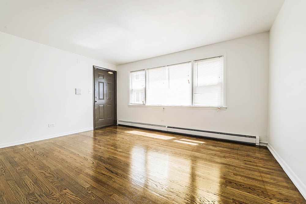 Empty room with hardwood floors, white walls, and a window with blinds.
