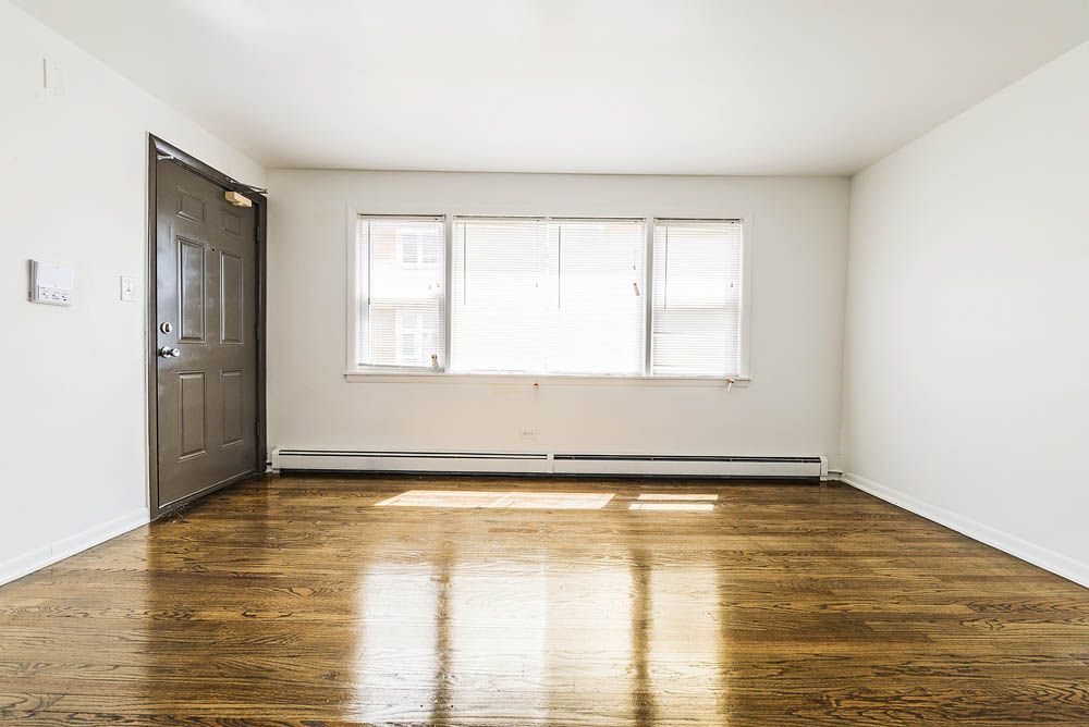 Empty room with hardwood floors, a door, and a window with blinds.