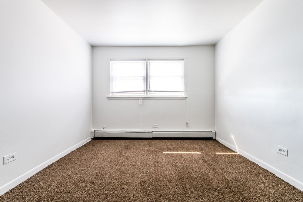 Empty room with brown carpet, white walls, and a window with blinds.