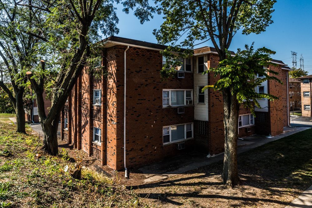 Brick apartment building with trees, sunlight, and blue sky.