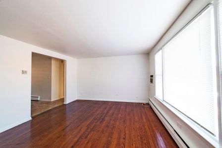 Empty living room with wood floors, large window, and doorway to another room.