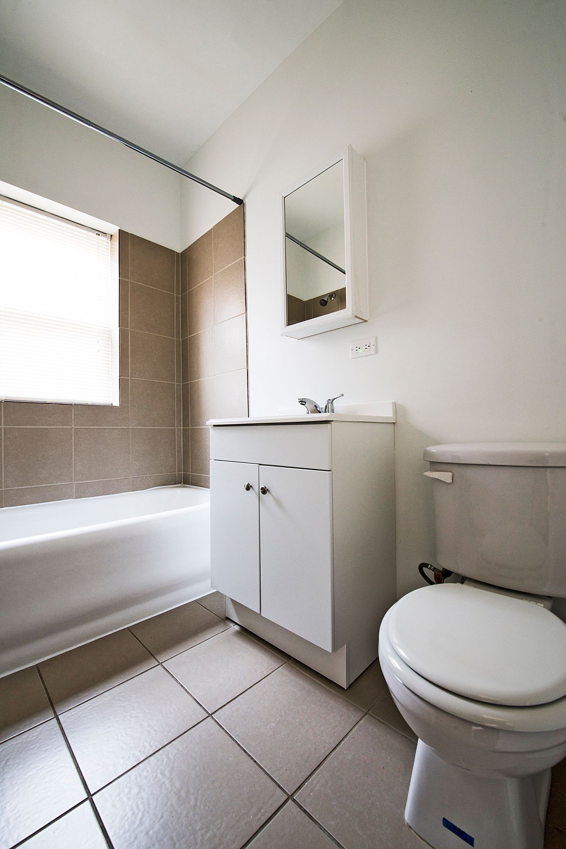 Bathroom with white cabinet, toilet, tub, and tan tile walls.