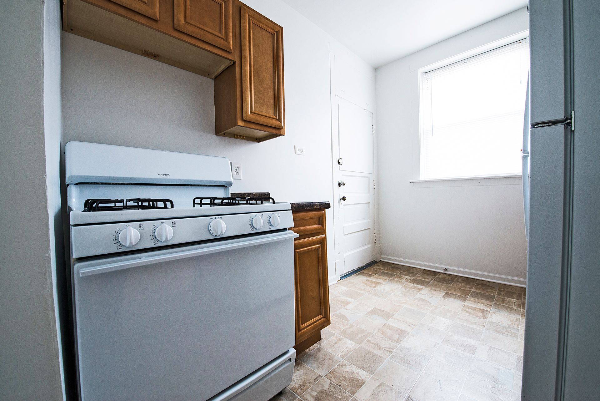 Kitchen with white stove, wooden cabinets, small window, and light-colored flooring.
