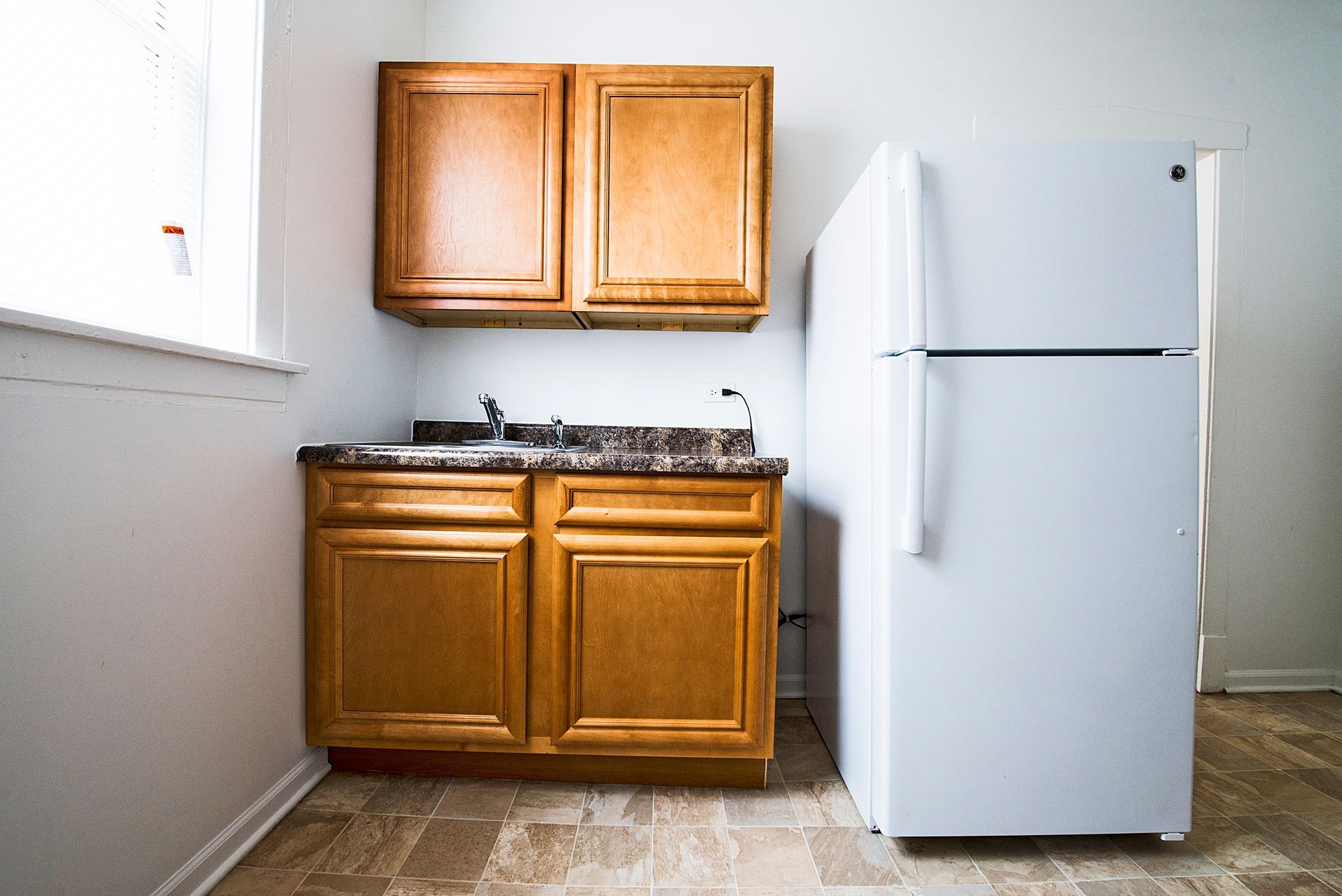 Small kitchen with wooden cabinets, countertop, sink, and white refrigerator.