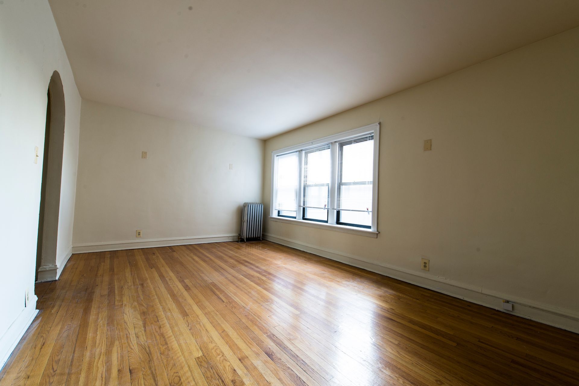 Empty room with hardwood floors, a large window, and an arched doorway.