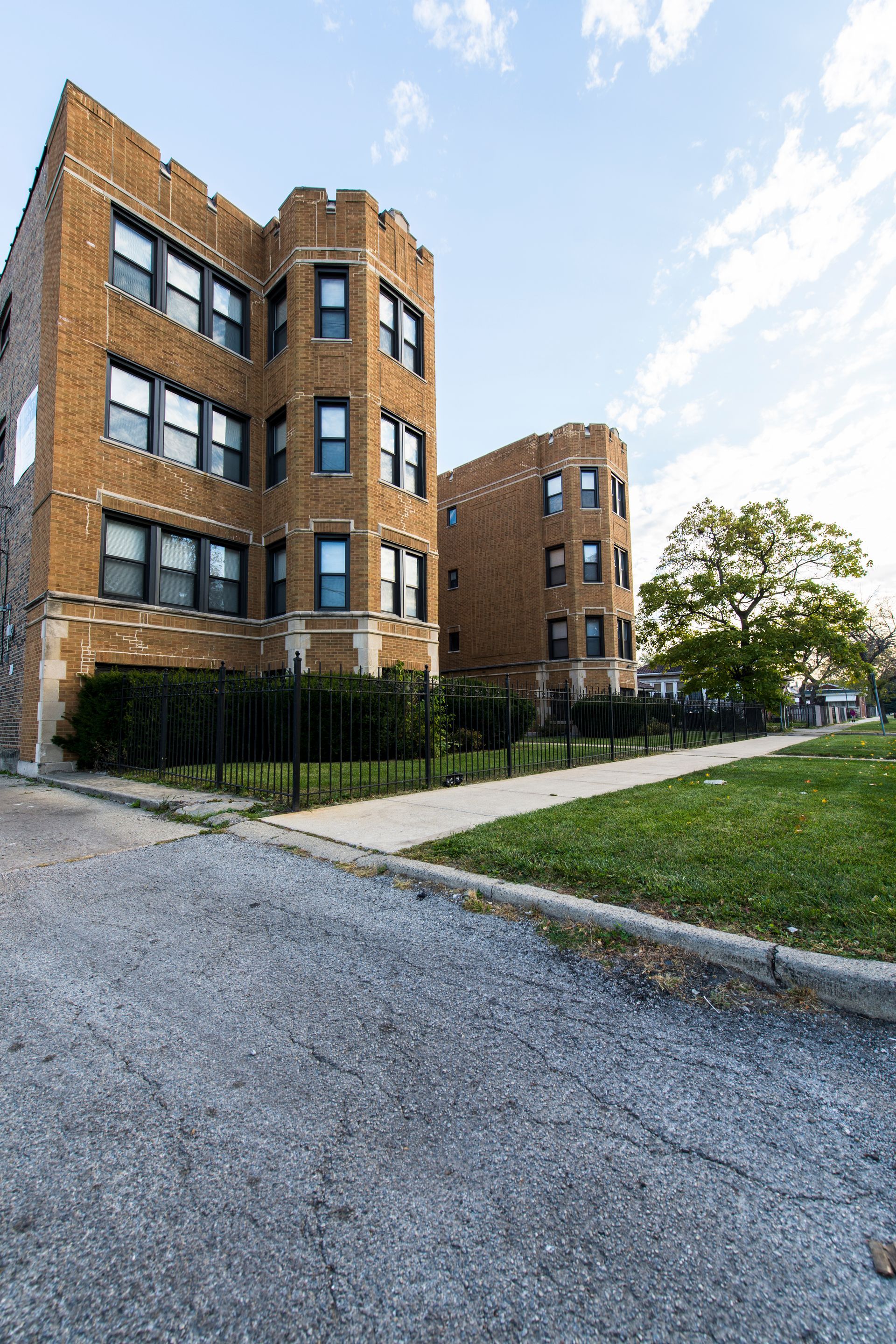 Brick apartment buildings with arched tops, sidewalk, and grassy area.