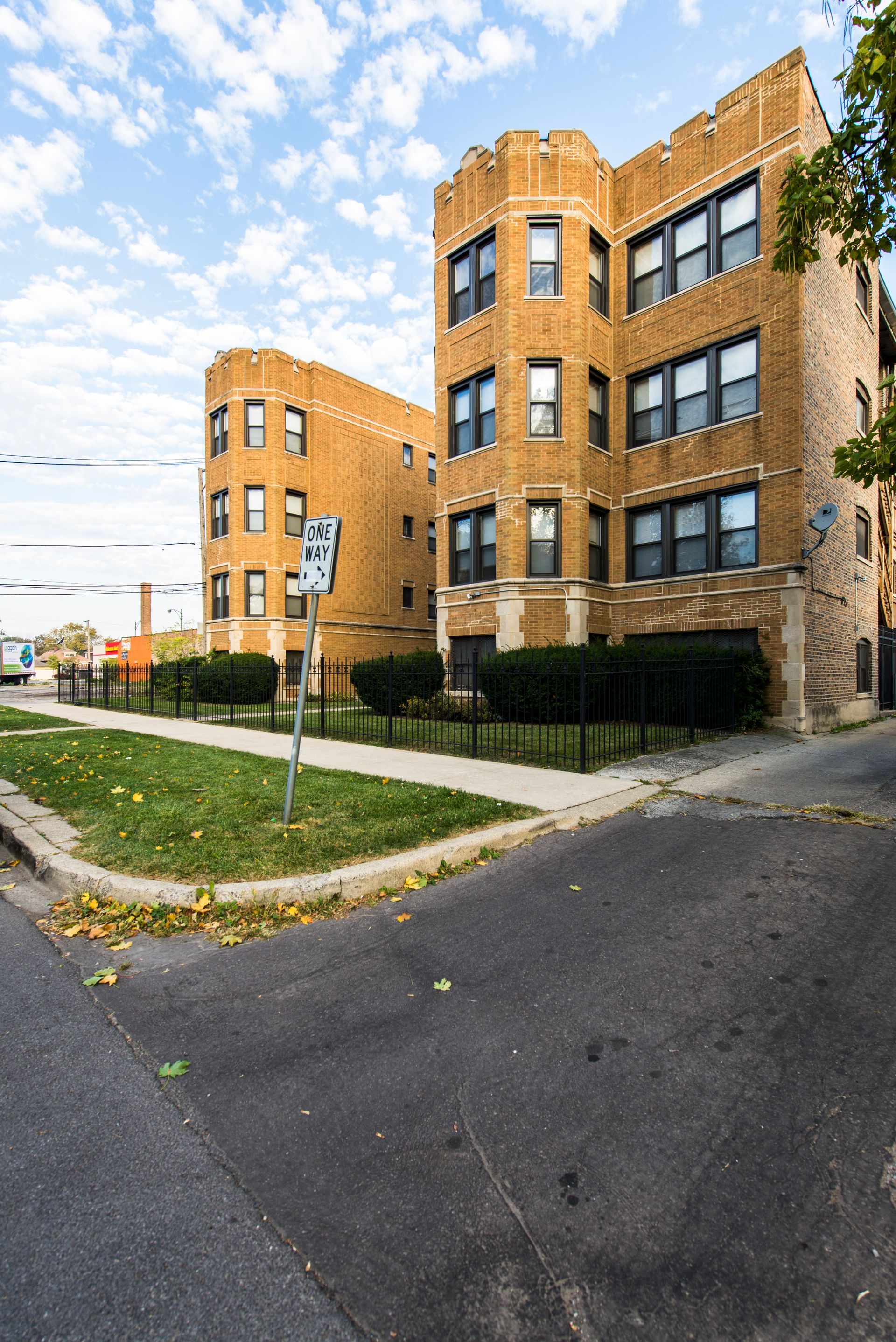 Brick apartment buildings on a street corner, with green grass and black fences.