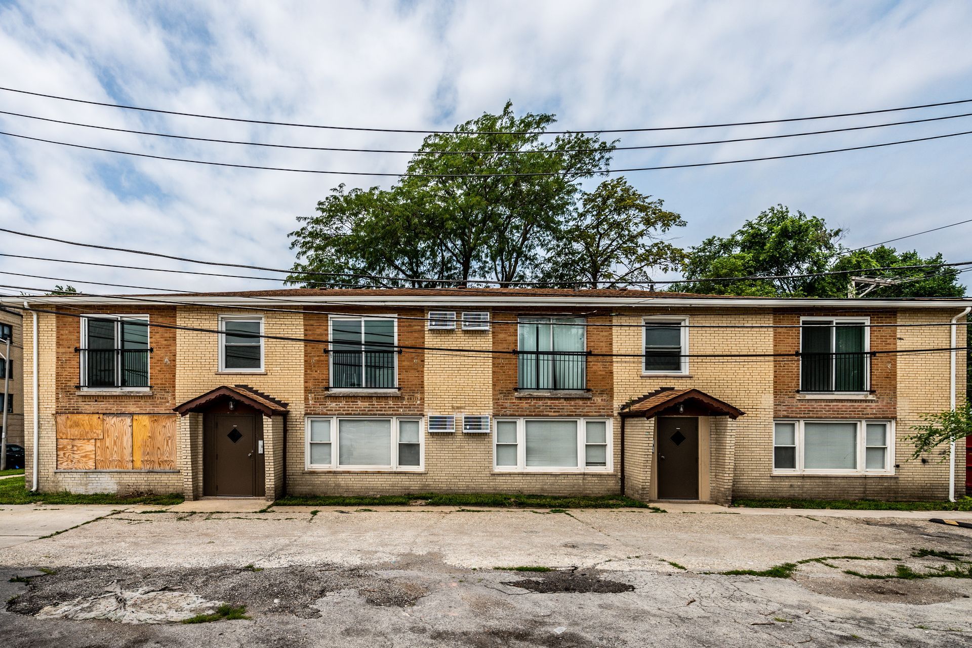 Two-story brick apartment building under a cloudy sky. Power lines are above the building.