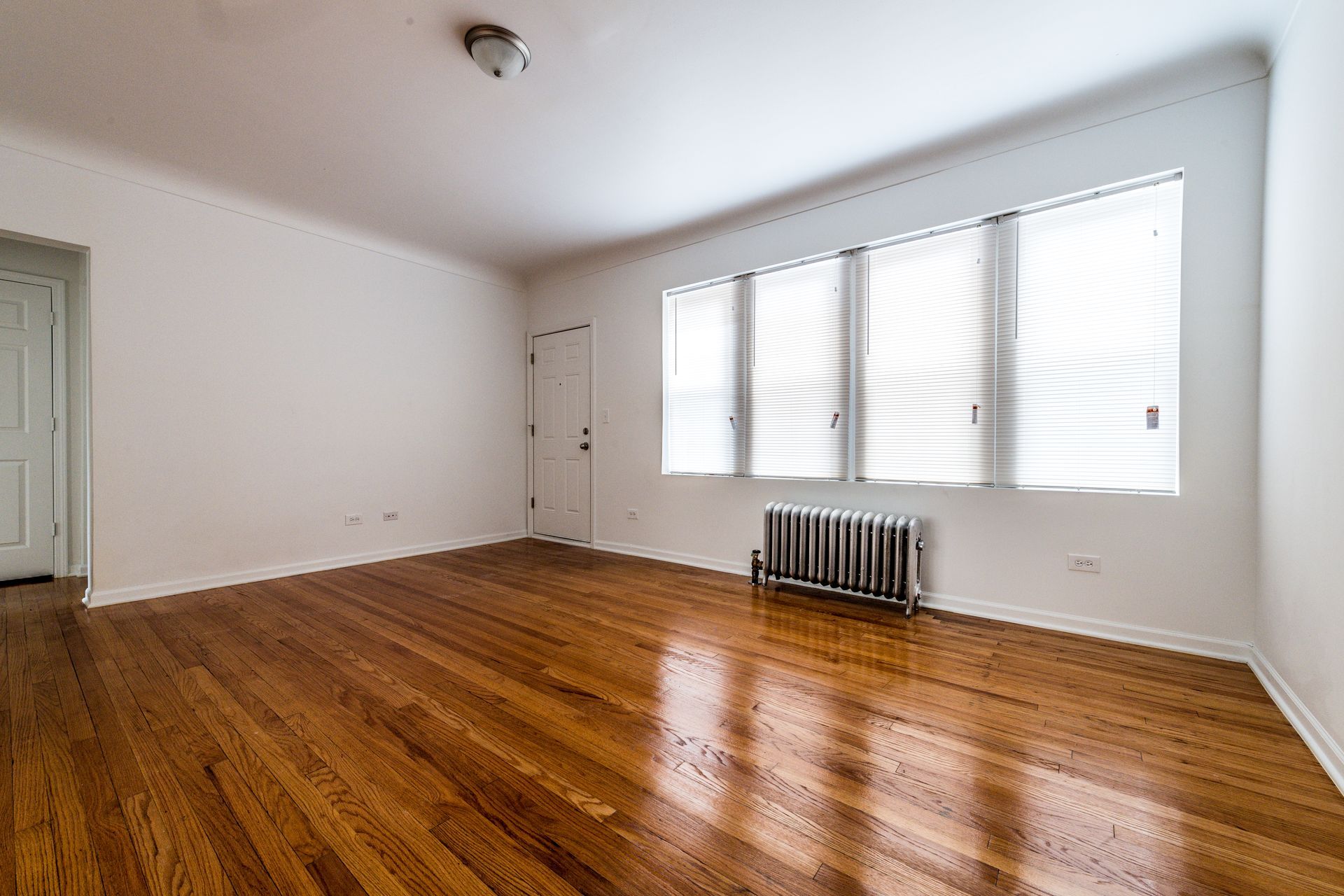 Empty room with wood floor, three windows with blinds, and a radiator.
