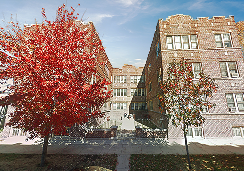 Two brick apartment buildings flank a walkway; red autumn trees frame the entrance.