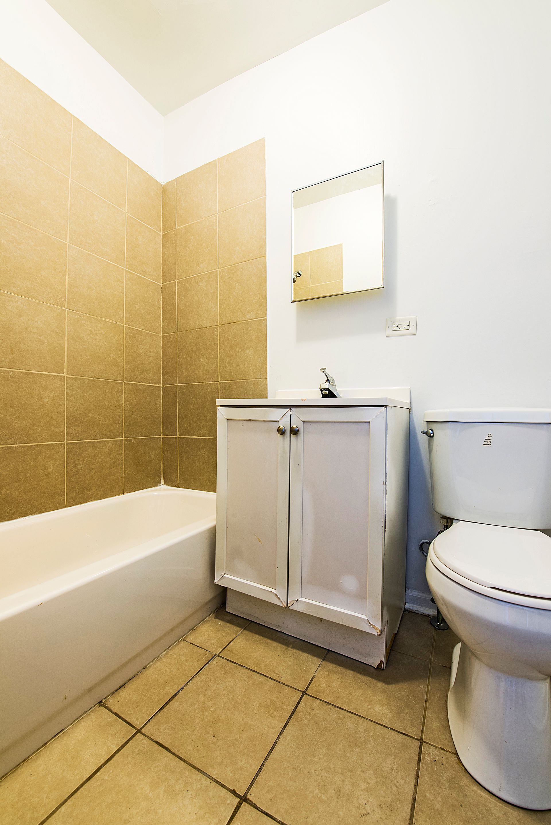 Bathroom with white fixtures, beige tile floor and wall. Cabinet and toilet are visible.