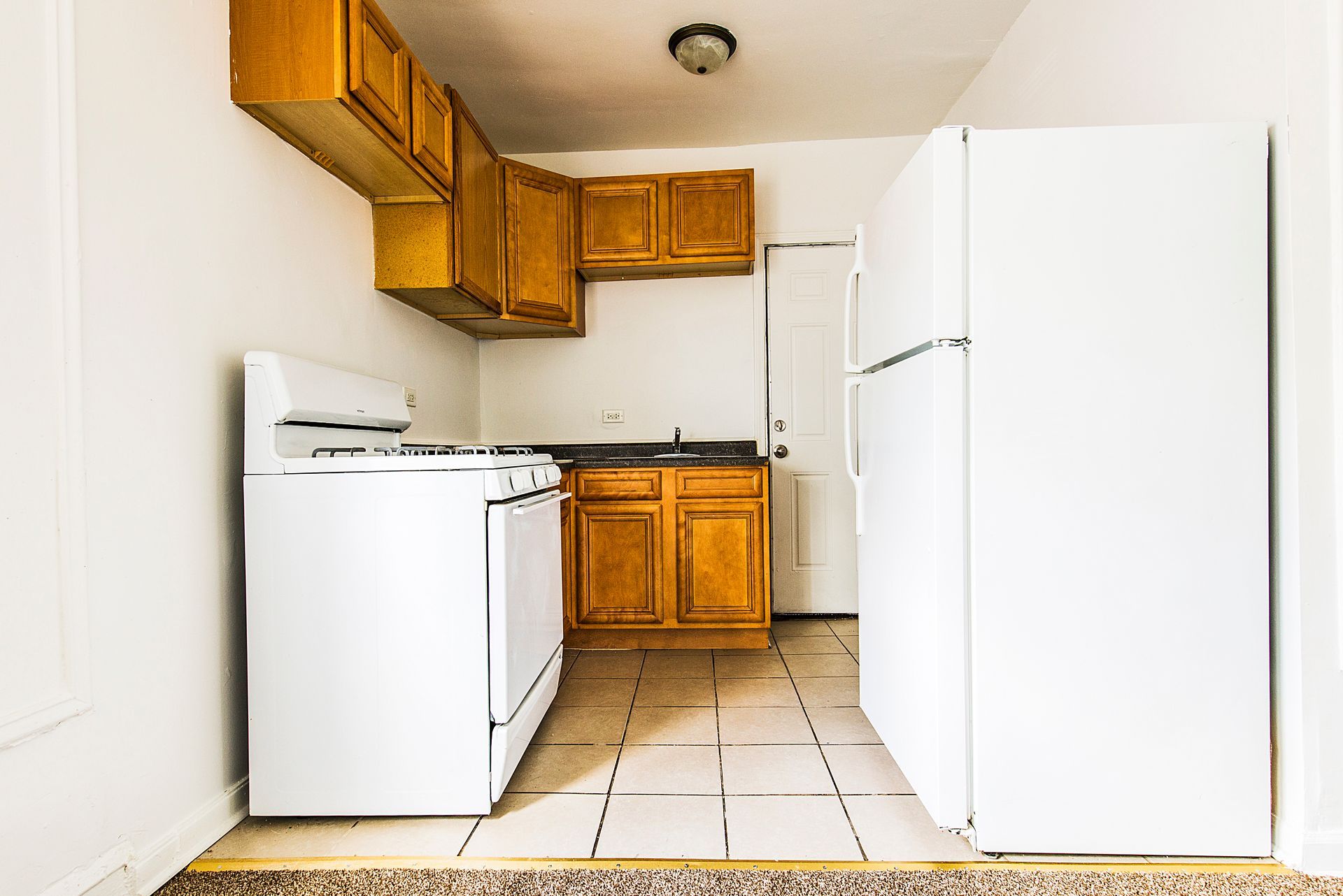 Small kitchen with white appliances, light wood cabinets, and tile floor.