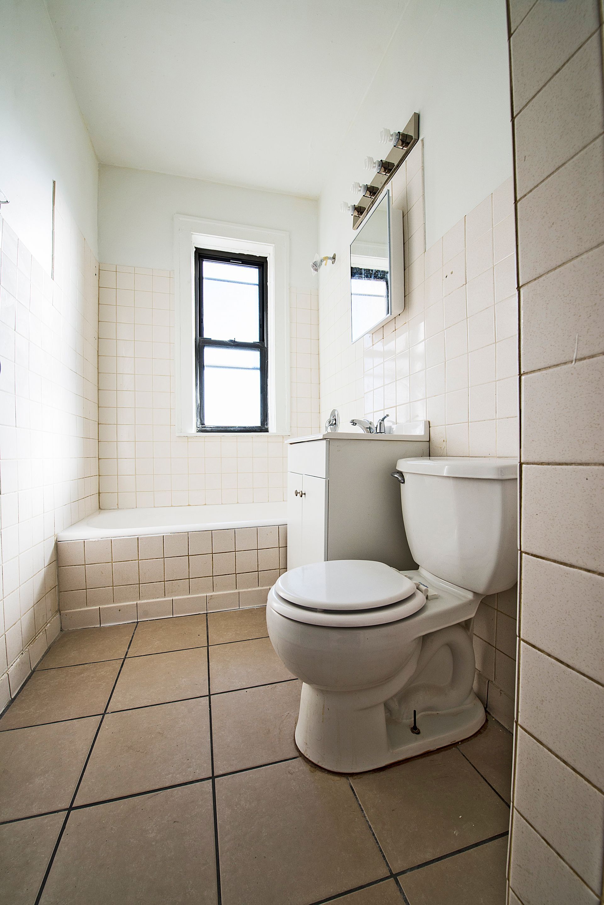 A small, tiled bathroom with a toilet, sink, and tub. The room is mostly white.