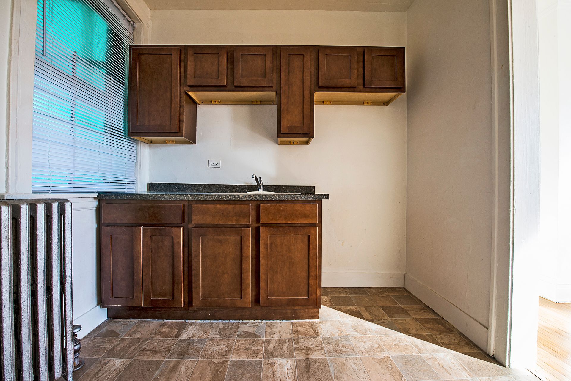 Empty kitchen with brown cabinets and countertop, radiator, and window.